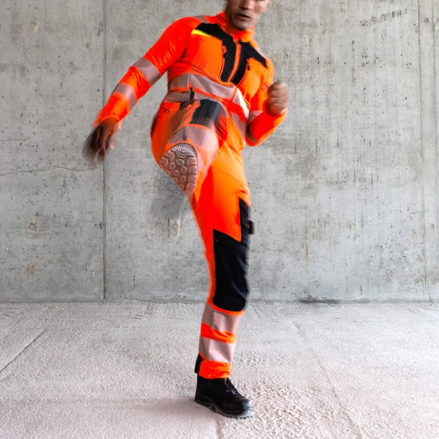 Trabajador con ropa de protecci&oacute;n naranja levantando una pierna en una patada.