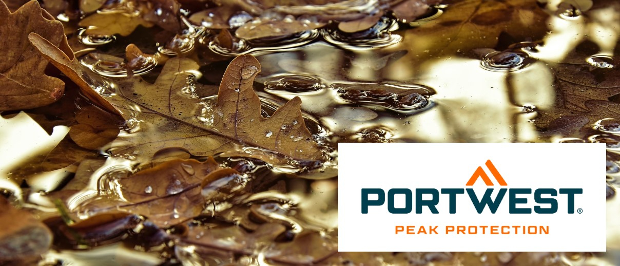 Imagen de un charco con hojas de roble marrón. El logo del fabricante Portwest se encuentra en la esquina inferior derecha de la imagen: blanco, fondo rectangular, escritura azul y naranja, doble triángulo naranja.