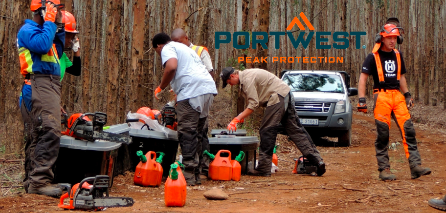 Trabajadores forestales en un claro preparándose para trabajar con motosierra. El logotipo del fabricante, Portwest, en azul y naranja, aparece centrado sobre la escena.