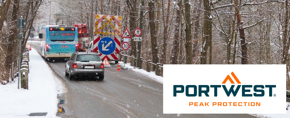 Escena de construcción con autobús y coche en una carretera nevada rodeada de árboles. En la esquina derecha está el logo de la marca Portwest.