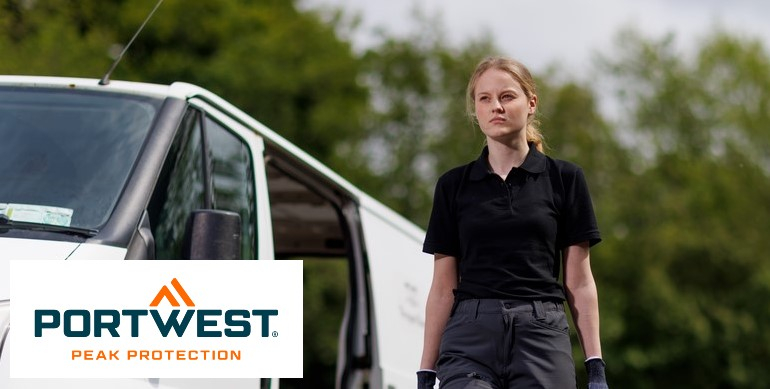 Una mujer vestida con una camisa polo negra y pantalones de trabajo grises se encuentra frente a una camioneta blanca al aire libre. Al fondo se ven árboles verdes. En la parte inferior izquierda de la imagen está el logo de "Portwest Peak Protection"