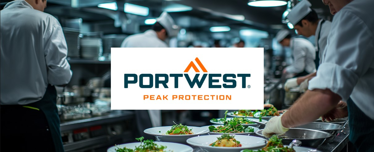 Una cocina comercial con varios chefs vestidos con uniformes blancos trabajando en diferentes estaciones y organizando la comida en platos. El enfoque se centra en platos recién preparados. El logotipo "Peak Protection" de Portwest está ubicado en el centro, encima de la imagen.