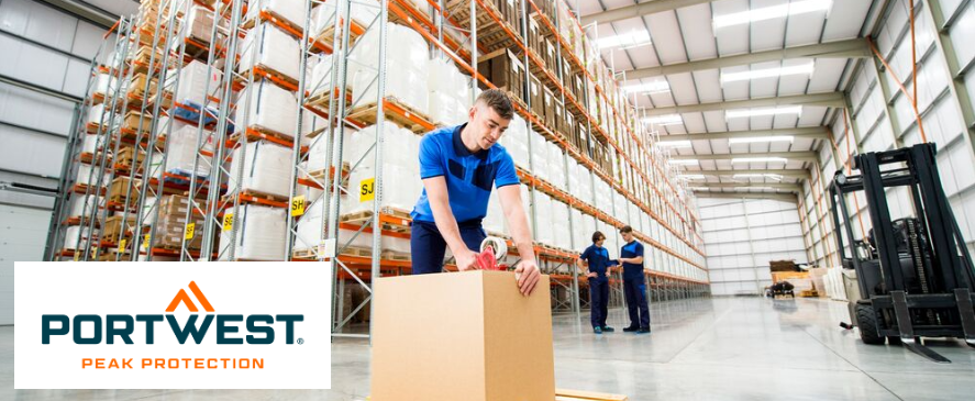 Un trabajador de almacén con ropa de trabajo azul cierra una caja grande con cinta adhesiva en un moderno y luminoso almacén de estanterías altas. Se puede ver a otros dos empleados charlando al fondo. El logotipo de Portwest con el eslogan "Peak Protection" aparece en la parte inferior izquierda de la imagen.