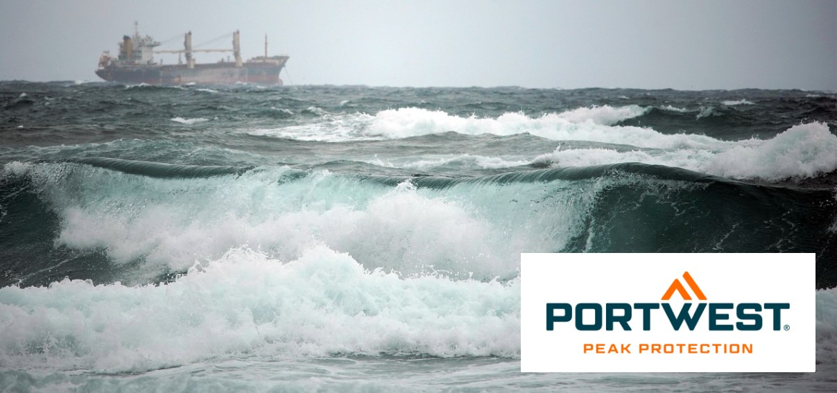 A lo lejos, un carguero navega por un mar tormentoso con olas altas cubiertas de espuma. En primer plano se pueden ver olas fuertes y turbulentas. El logotipo de Portwest está en la parte inferior derecha de la imagen.