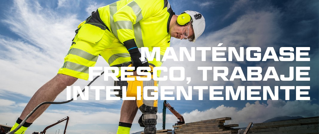 Trabajador con casco y protección auditiva en ropa de trabajo de verano amarilla de alta visibilidad trabajando con un martillo neumático, en el fondo azul, cielo ligeramente nublado, excavadora y pila de tablones de madera.