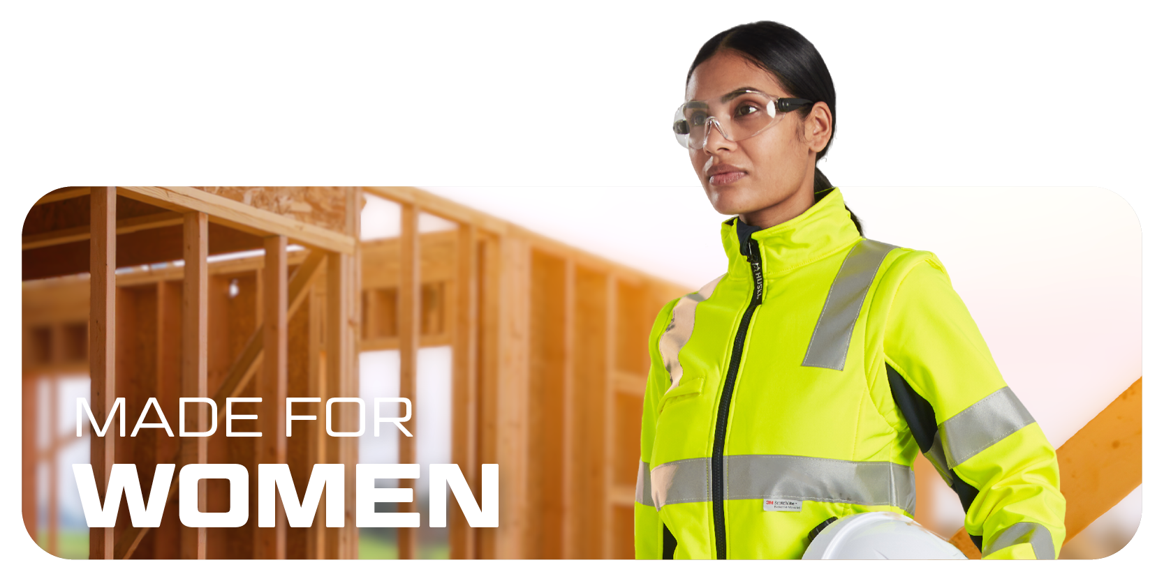 Señora con gafas, casco y ropa de advertencia, al fondo paredes de madera en construcción de postes y vigas.