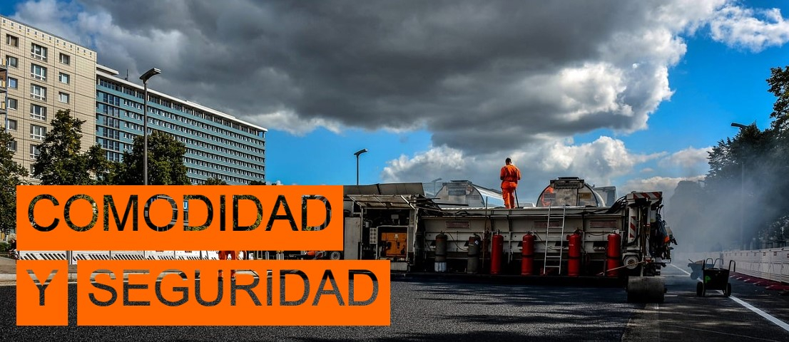 Escena de una obra de construcción de carreteras. A la izquierda de la imagen se pueden ver edificios altos y algunos árboles, la parte derecha de la imagen está cubierta por una fuente de agua. En el borde inferior izquierdo de la imagen se encuentran las palabras “Comodidad y Seguridad” en letras recortadas con un fondo naranja.
