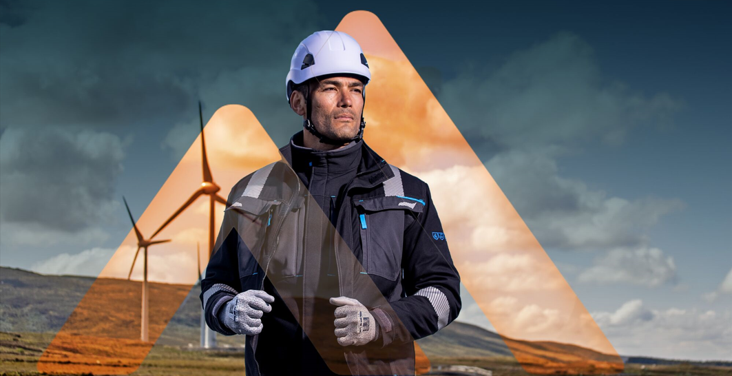 Un hombre con casco, guantes y chaqueta de trabajo se encuentra frente a aerogeneradores; ilustración de seguridad laboral y protección contra caídas al trabajar en altura.