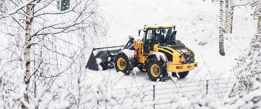 Tractor amarillo con pala en un paisaje nevado con vallas y abedules.