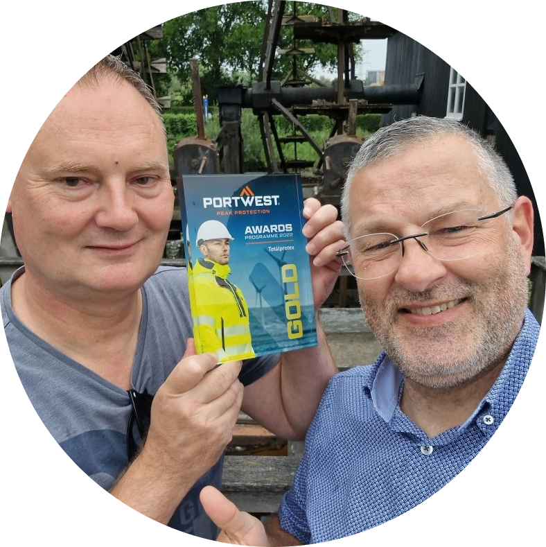 Sjoerd Kusters y Patrick Kits en un entorno rural. Los hombres sonríen a la cámara, Sjoerd sostiene la placa dorada en sus manos, Patrick levanta el pulgar derecho.